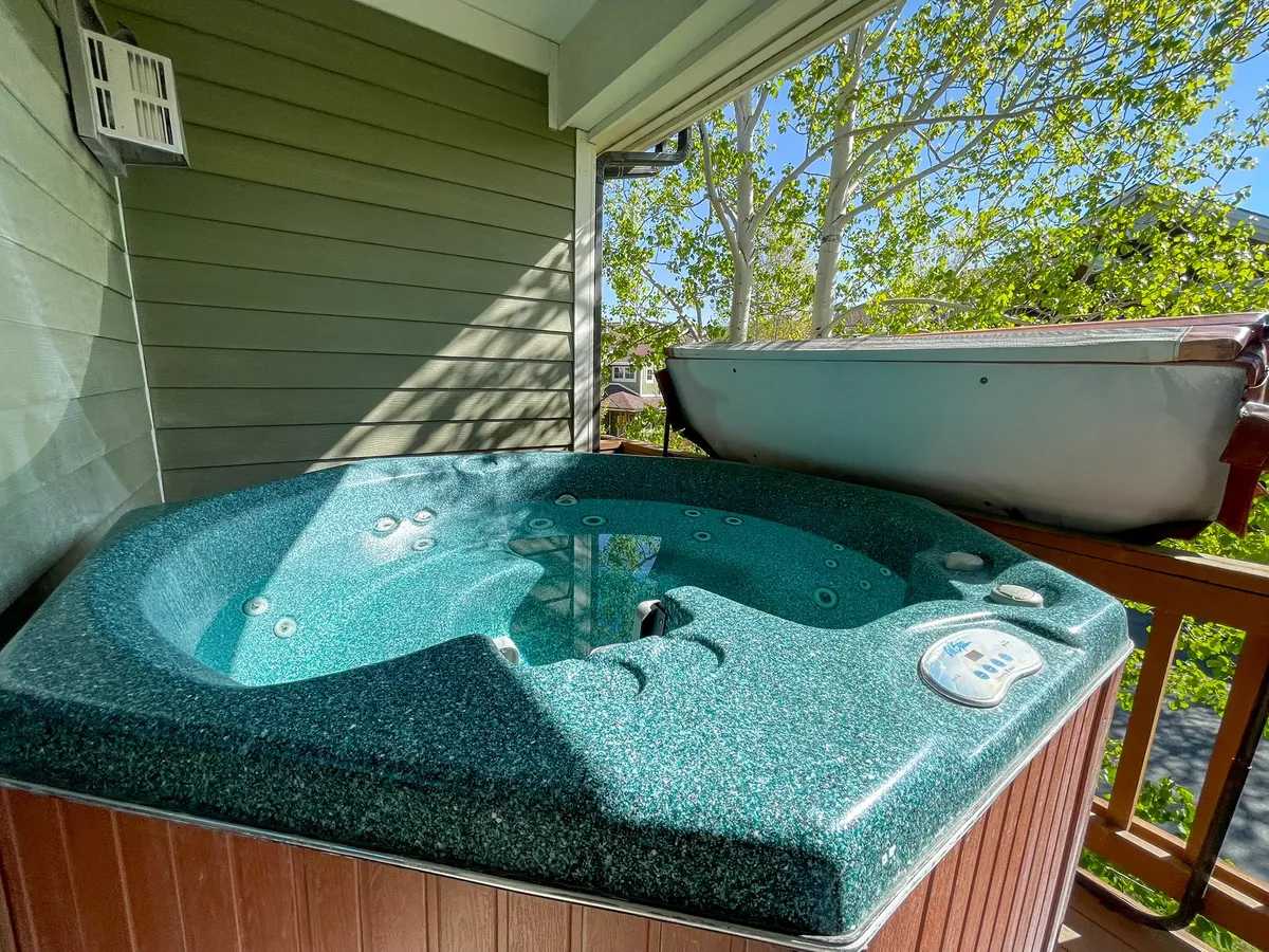 A tranquil deck with a hot tub bordered by lush greenery and a secure railing, inviting guests to soak while gazing at the natural scenery. The space is presented in soft, flattering light, emphasizing relaxation and privacy.