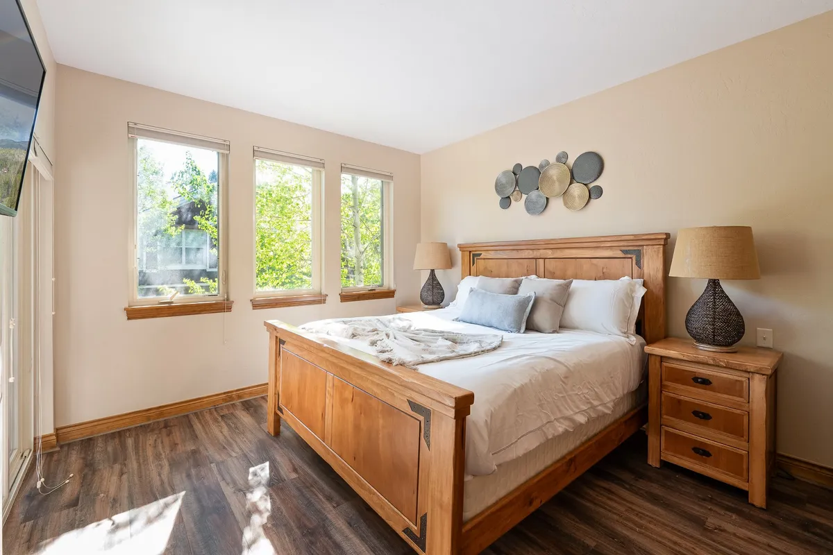 A bright and tranquil bedroom featuring a comfortable bed, stylish decorative wall art, a cozy nightstand with a lamp, and sunlit window views. The overall atmosphere is peaceful and inviting, ideal for restful sleep and relaxing mornings.