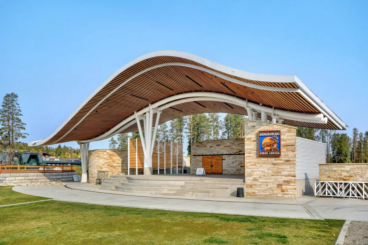 An exterior view of a curved-roof event center with a stone facade and steps leading to a stage, highlighting the space used for live performances, festivals, and community gatherings. The sign for the event center is visible, emphasizing its role as a local hub.