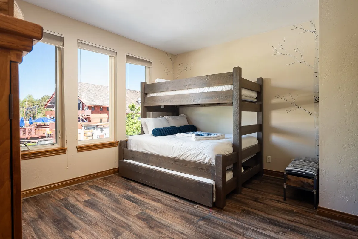 A cozy bunk room with a twin-over-queen bunk bed, large windows that fill the space with natural light, and playful wooden accents. Decorative wall branches add a whimsical touch, and the room feels welcoming for both kids and extra guests.