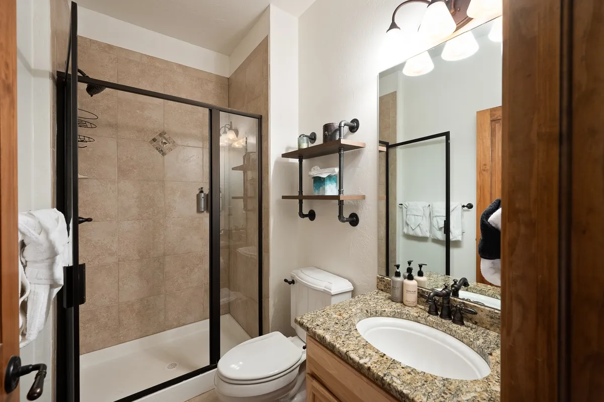 A modern bathroom with a glass-enclosed shower, granite countertop, large mirror, and neatly arranged shelves. The space feels serene and functional, ideal for refreshing showers or moments of relaxation.