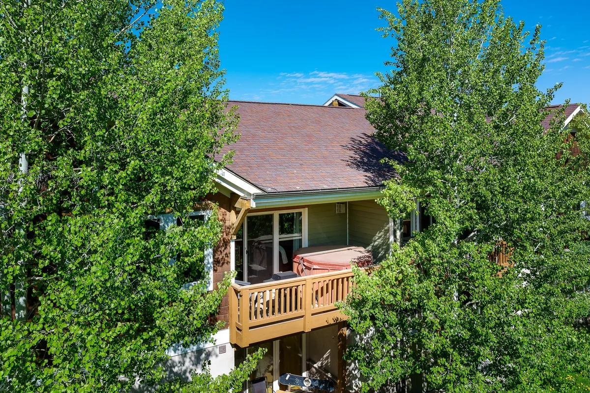 A serene exterior balcony with a hot tub, surrounded by trees and topped by a peaceful roof. The balcony offers seating and space for al fresco meals, with mountain views and opportunities for relaxation in the fresh air.