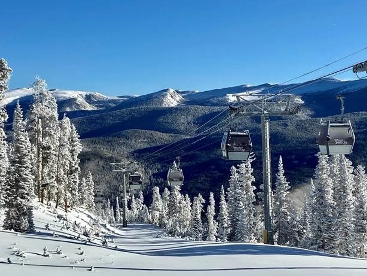 This exterior image showcases snow-covered ski slopes, ski lift gondolas, and distant mountain vistas framed by pine trees. The scene captures the quintessential winter experience in the Rockies, evoking adventure and tranquility.