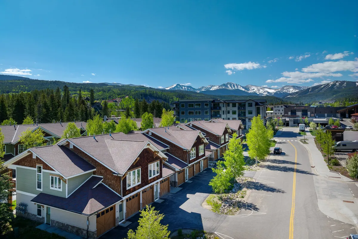 A welcoming exterior image showcasing a row of houses along a tree-lined street with a dramatic mountain range in the background. The inviting scene suggests easy access to both community life and outdoor adventures.