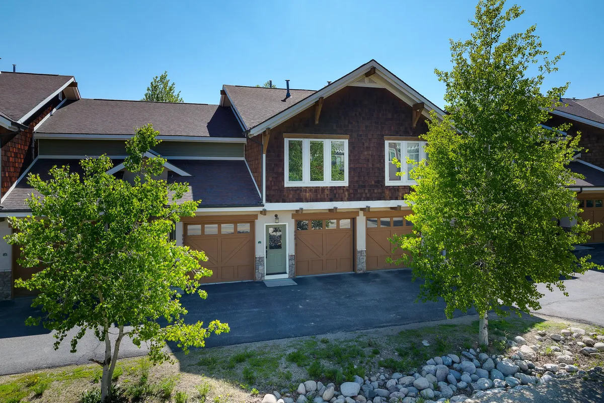 A welcoming exterior shot of the home’s front entrance framed by trees, showing garage doors and a porch. The setting is serene, suggesting privacy and comfort in a residential neighborhood.