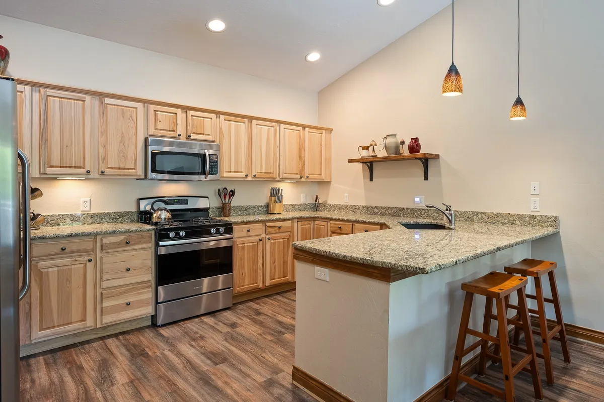 A warm, inviting kitchen space featuring granite countertops, stainless steel appliances, wooden cabinetry, and pendant lighting. The area is styled for cooking and entertaining, with ample workspace and comfortable lighting that encourages family interaction.