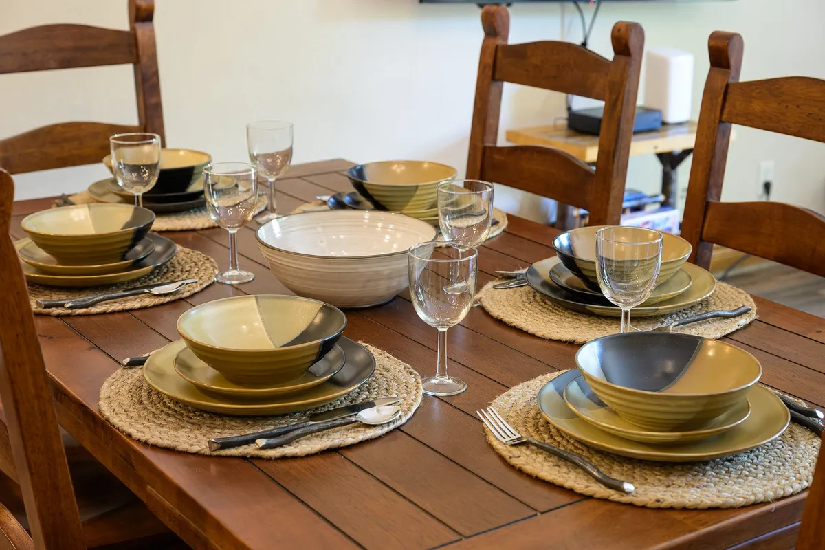 A warmly lit dining area is set with elegant place settings, decorative bowls, and glassware, all arranged on a stylish table. The space is inviting, ideal for intimate gatherings, gourmet meals, or celebrations, fitting the narrative of memorable, shared experiences in a luxurious retreat.