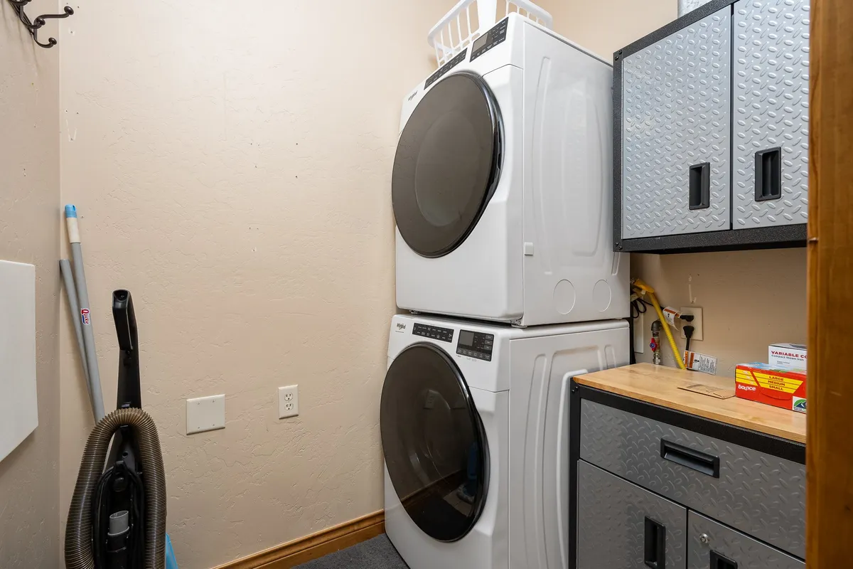 A compact laundry area indoors, equipped with a stacked washer and dryer, storage cabinets, and essential cleaning supplies. The space is organized and practical, emphasizing home convenience.